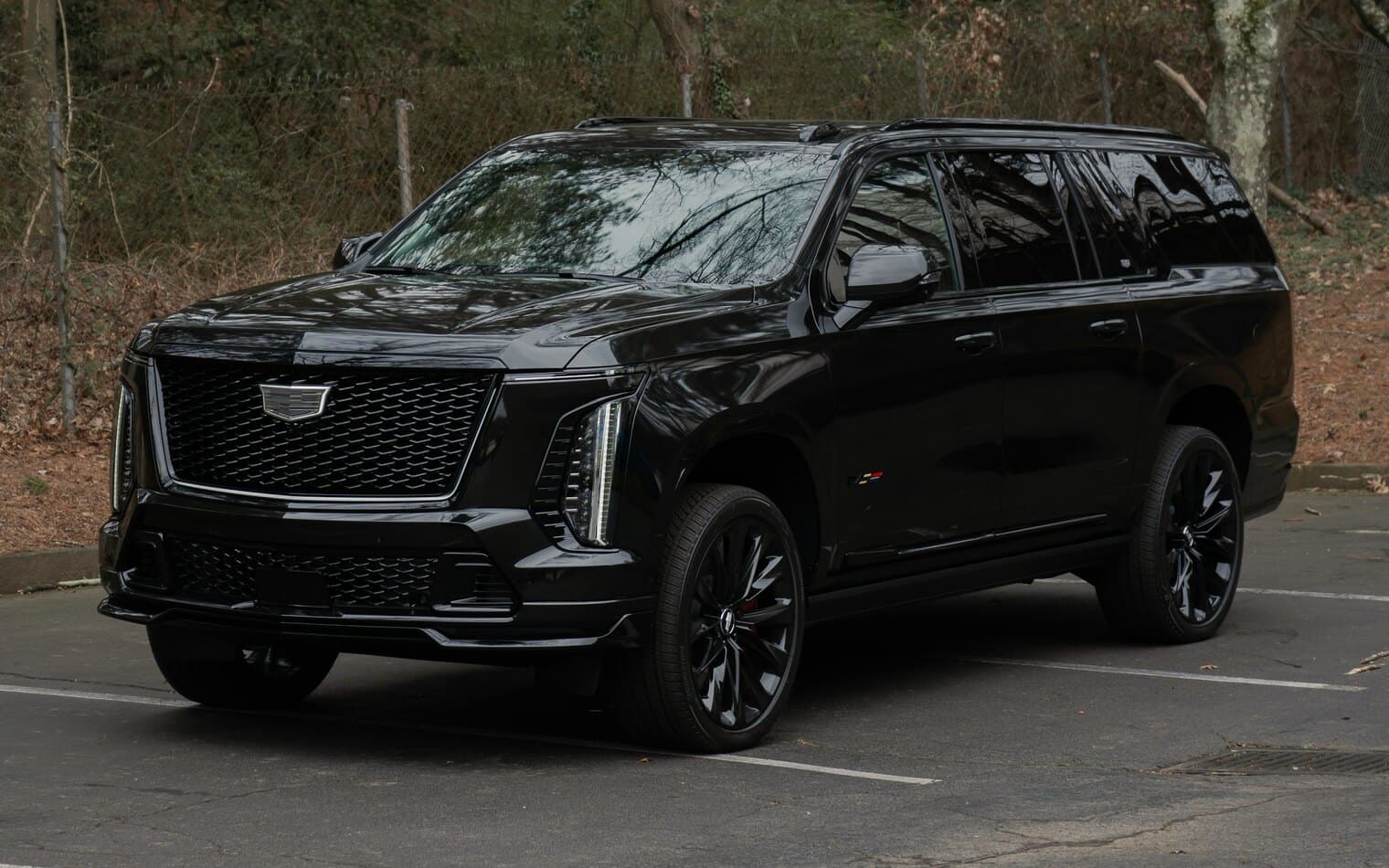 A black full-size SUV parked beside a wooded lot in daylight